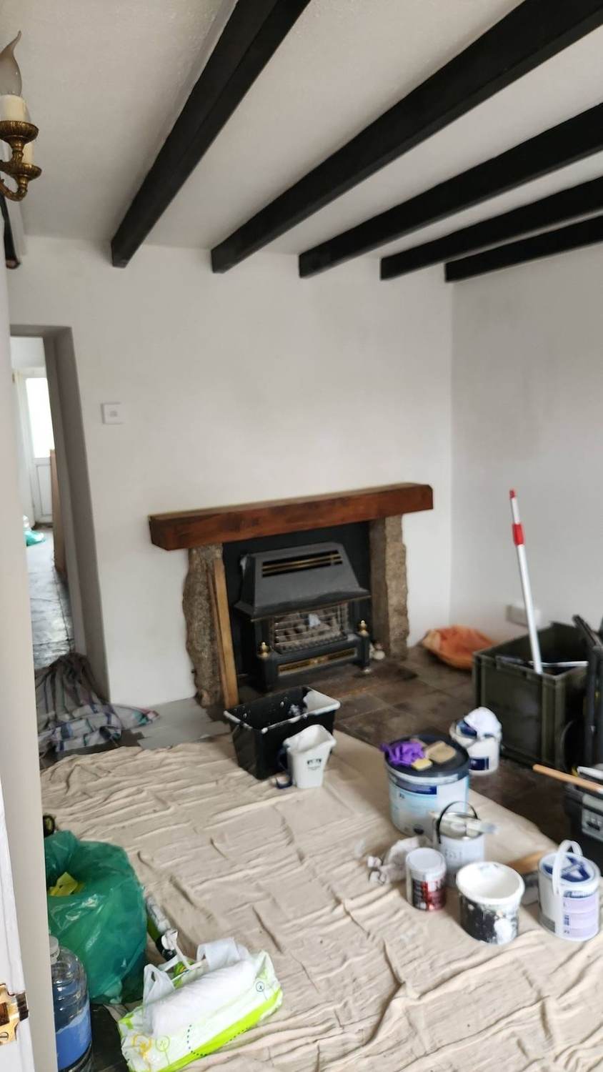 Cottage interior prepped for repaint — exposed black beams and stone fireplace