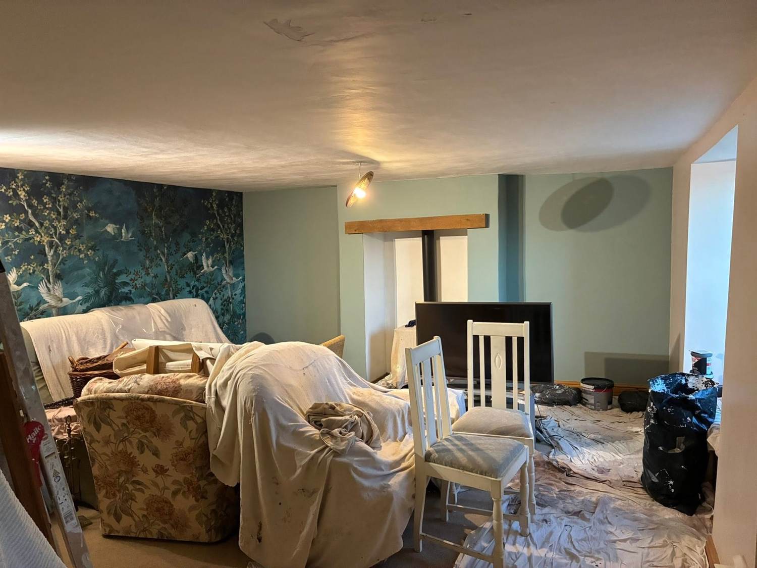 Sitting room mid-redecoration — furniture sheeted, heron feature wall and woodburner